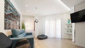 Een moderne woonkamer met een bank, een relax fauteuil, een flatscreen televisie en een groot schilderij aan de muur.