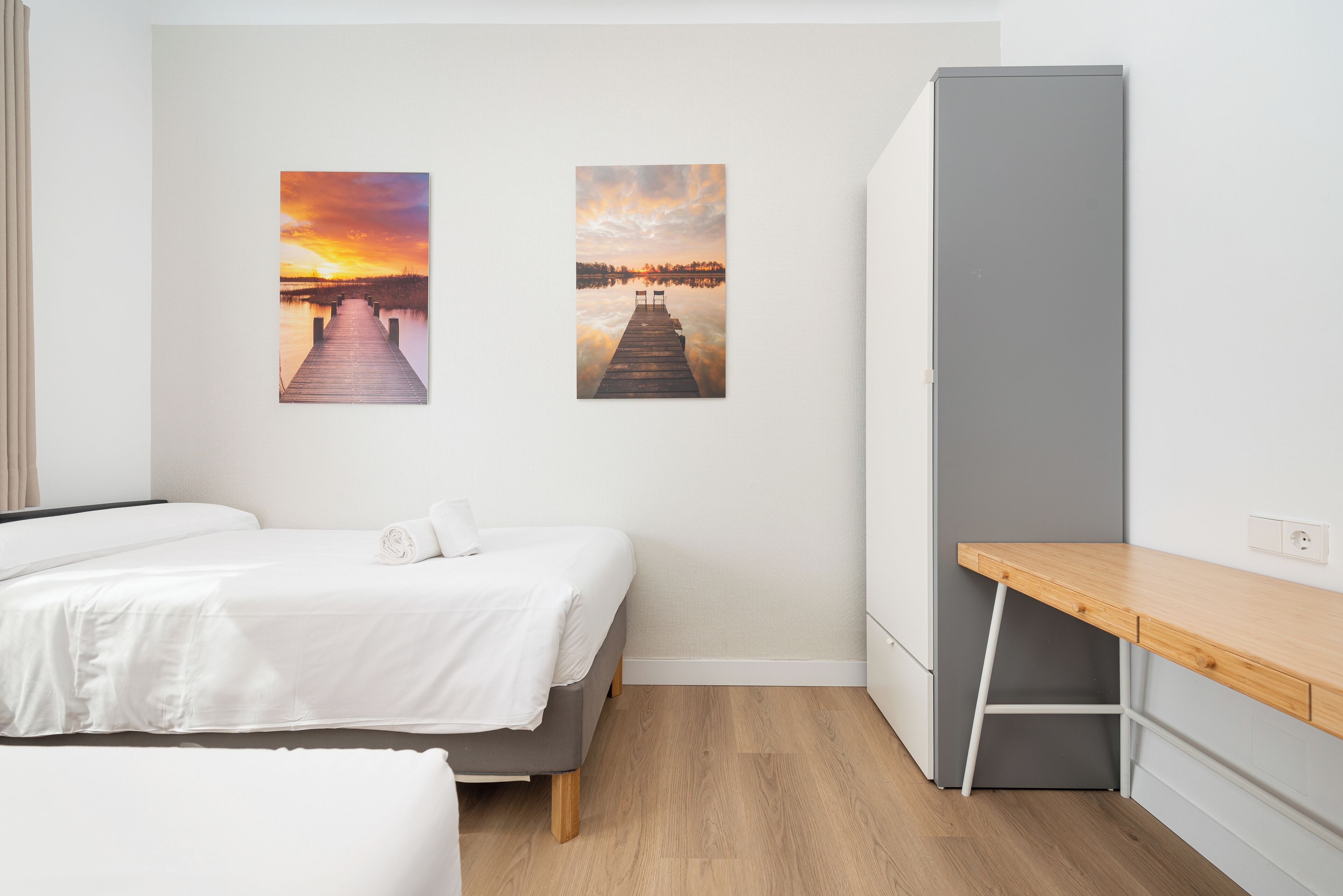 Une chambre à coucher avec un lit, un bureau et deux tableaux représentant un coucher de soleil accrochés au mur.