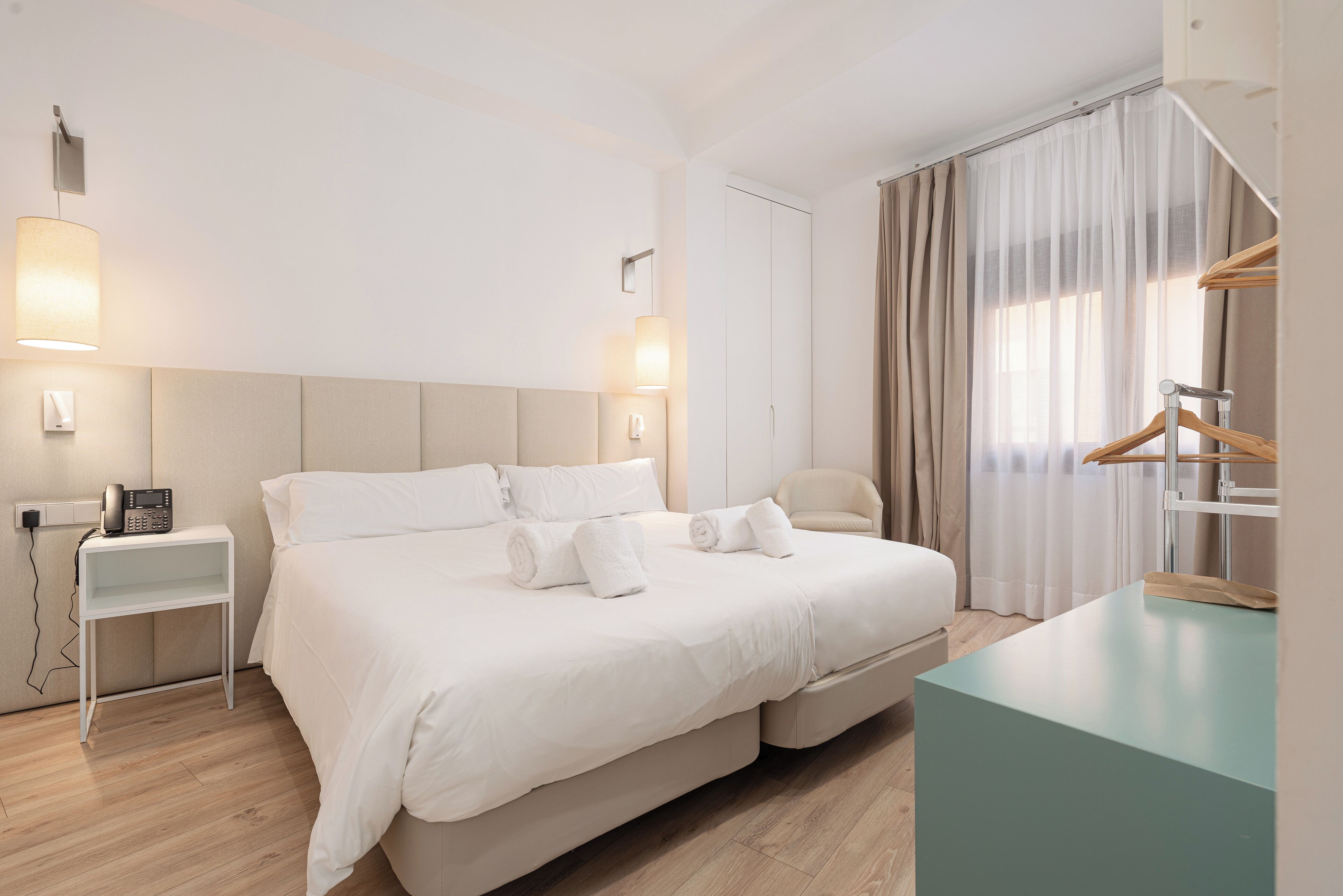Et moderne hotelværelse med en stor seng, sengeborde, et skrivebord og et klædeskab.