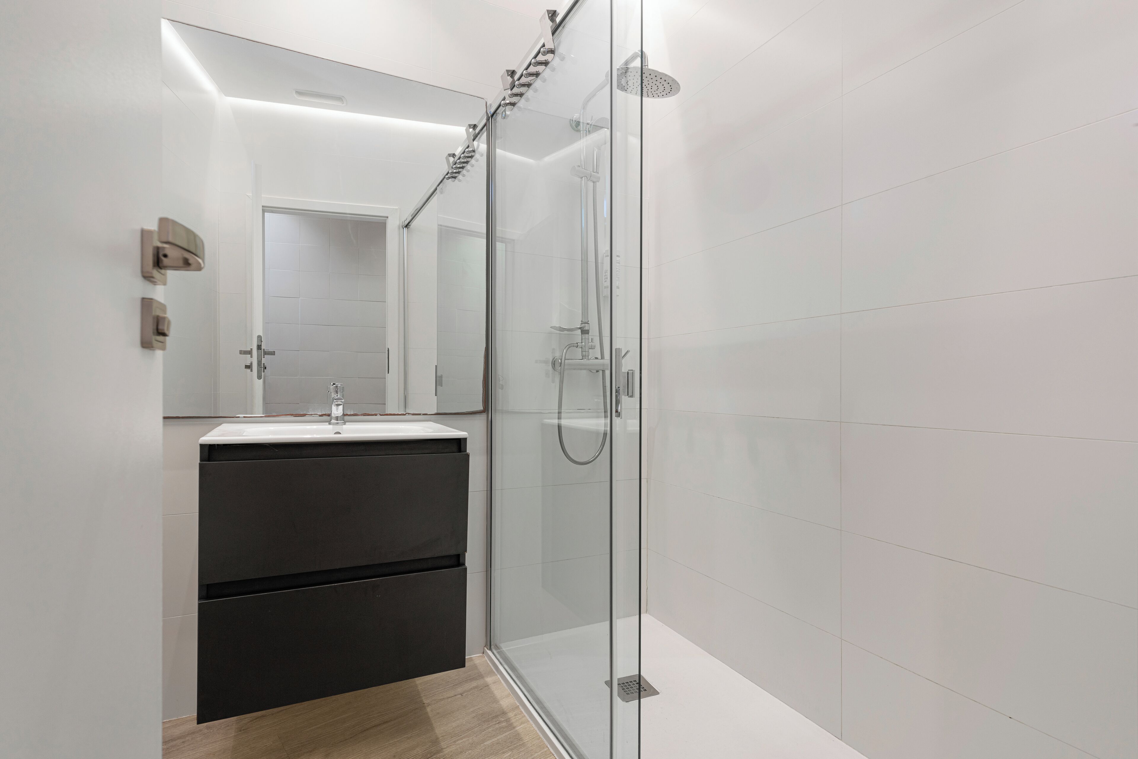 A modern bathroom with a glass shower enclosure, a sink with a mirror, and a dark-colored vanity.