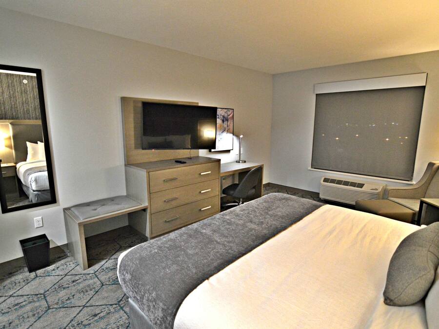 A hotel room with a large bed, a desk with a computer, a television, and a mirror.