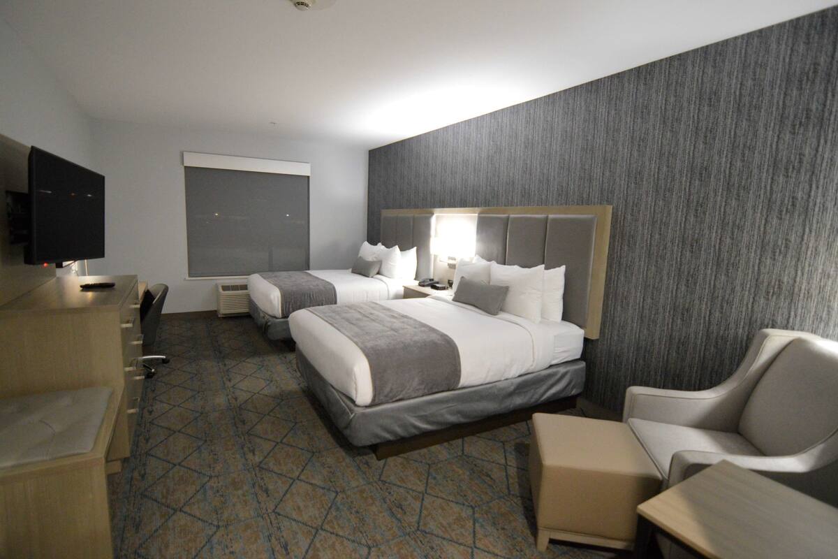 A hotel room with two beds, a desk, a TV, and a large window.