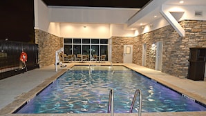 An indoor swimming pool with clear water, stone walls, and a seating area with chairs.