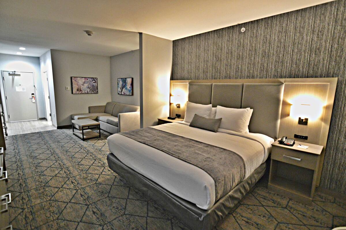 A hotel room with a large bed, two bedside tables, a sofa, and a patterned carpet.