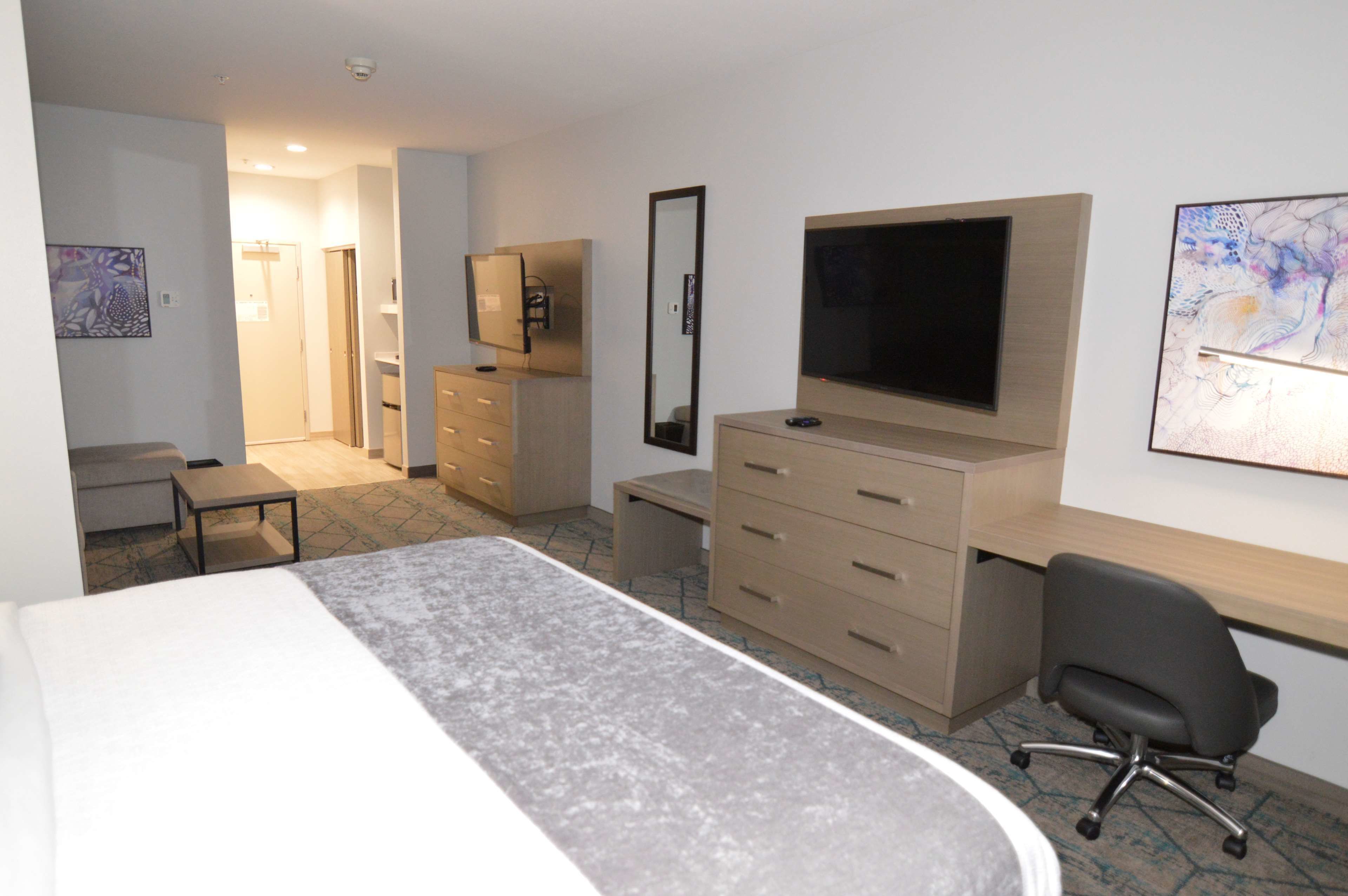 Ett hotellrum med en säng, ett skrivbord, en stol, en tv, en byrå och en spegel.