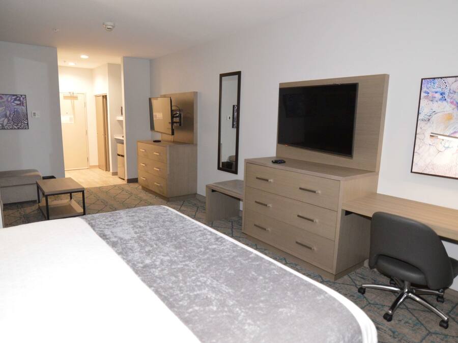 A hotel room with a bed, a desk, a chair, a TV, a dresser, and a mirror.