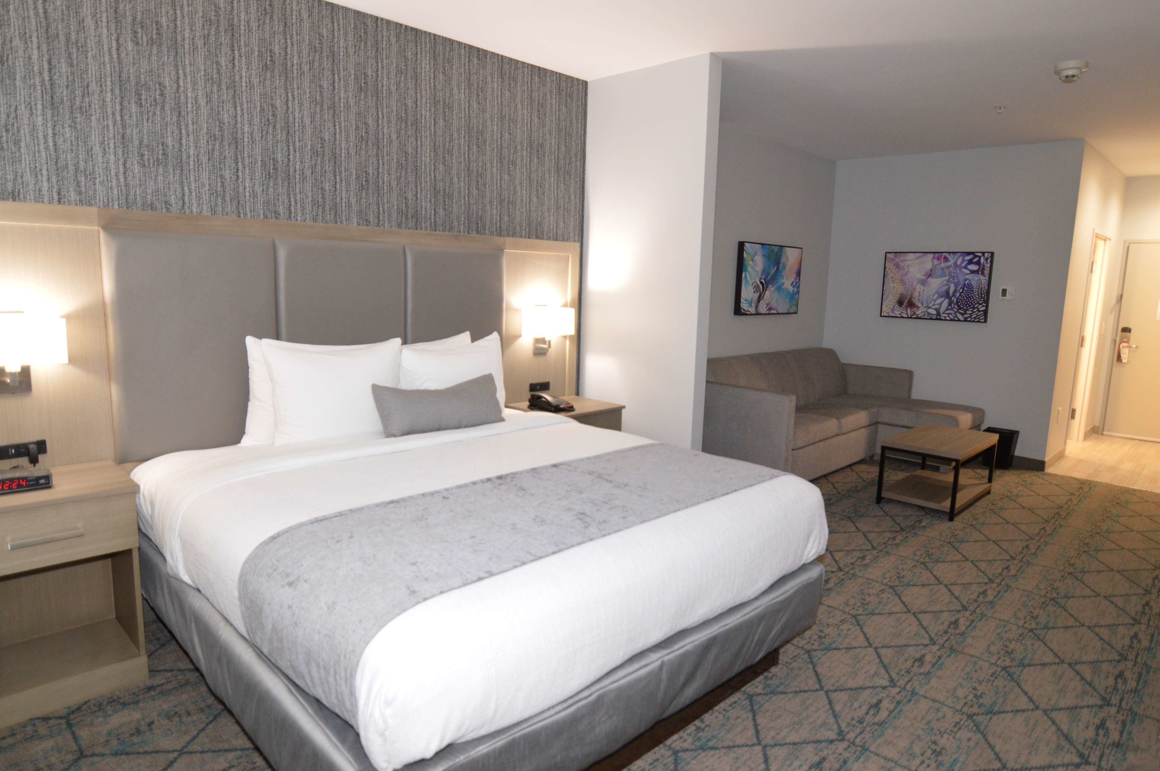 Une chambre d’hôtel avec un grand lit, un canapé, une table basse et deux lampes fixées au mur.