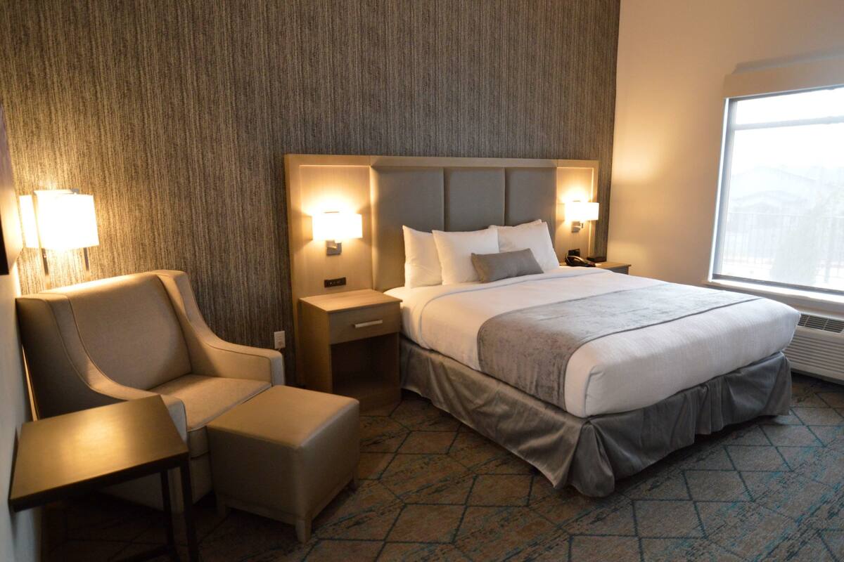 A hotel room with a large bed, two bedside tables with lamps, a chair, and a small table.