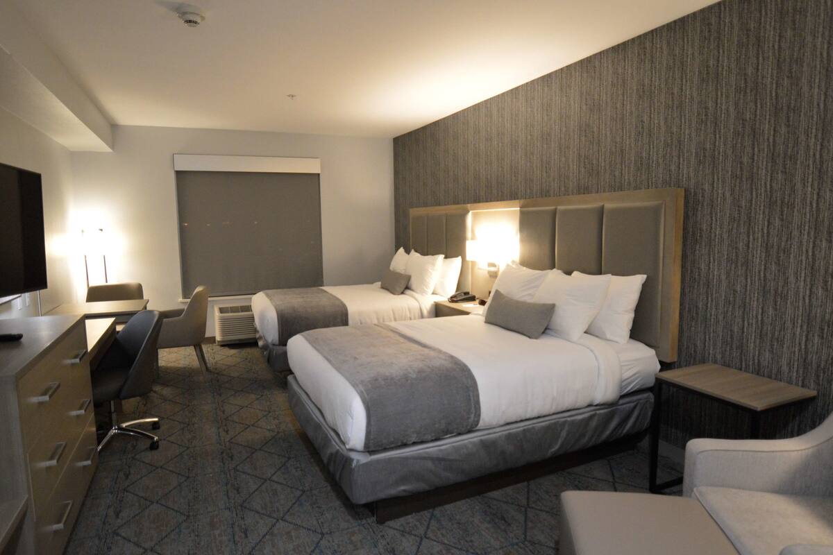 A hotel room with two beds, a desk, a chair, and a TV.