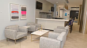 A modern living area with grey patterned sofas, a white coffee table, and a kitchen area with a bar.
