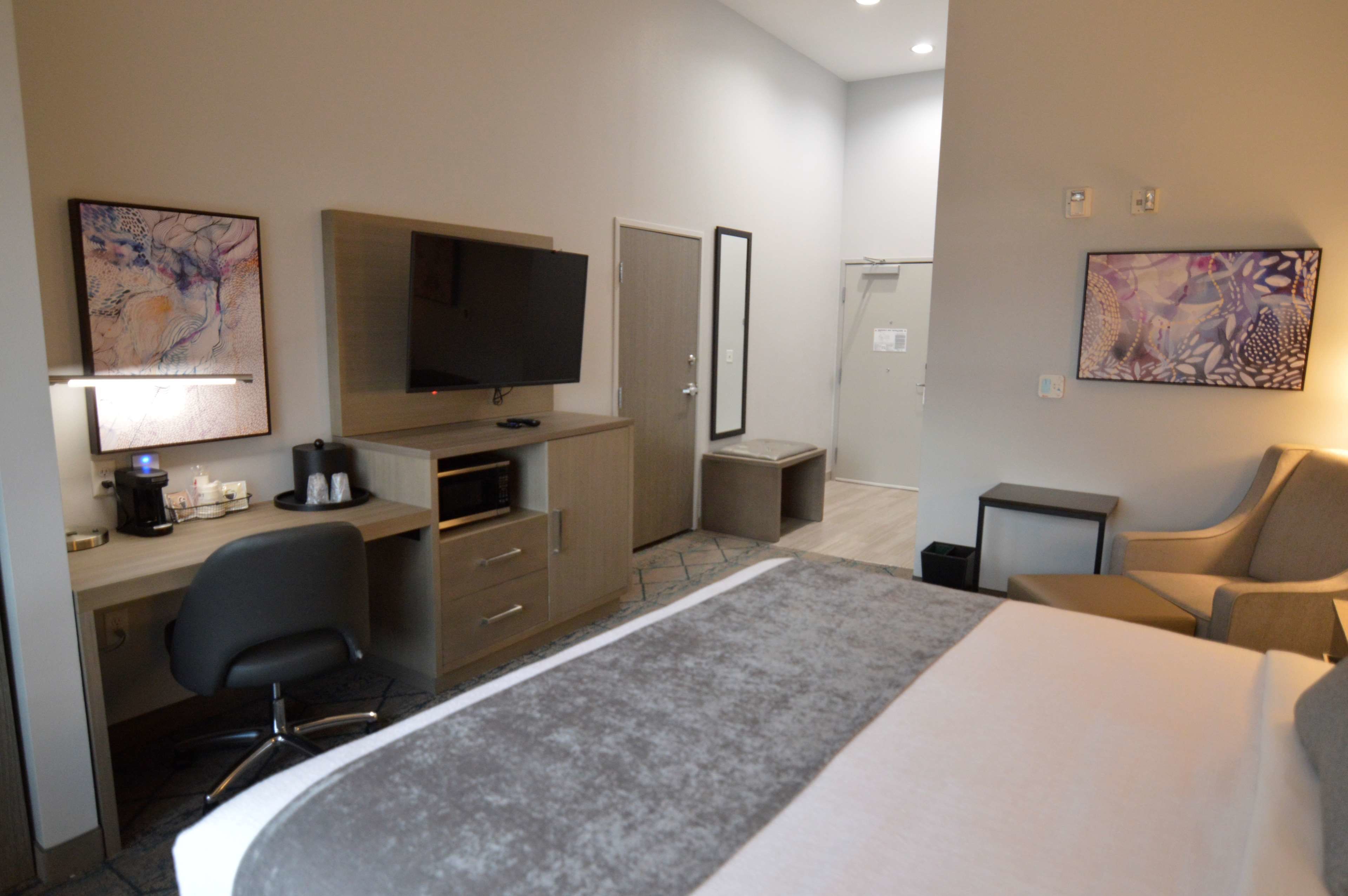 A hotel room with a bed, desk, chair, television, and artwork on the walls.