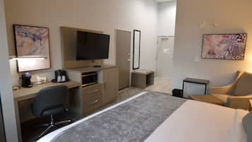 A hotel room with a bed, desk, chair, television, and artwork on the walls.