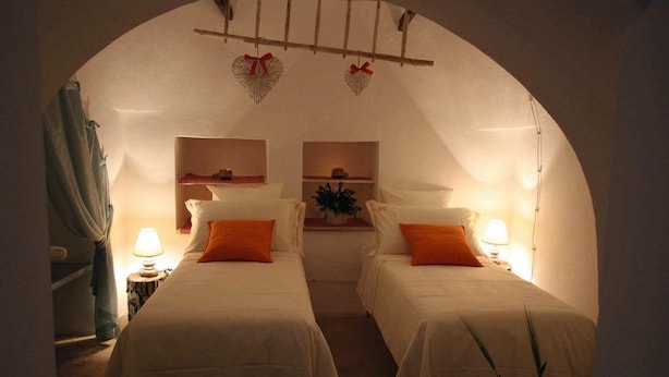 A cozy room with two beds, each with white bedding and orange pillows, under a vaulted ceiling with heart-shaped decorations. - Suite del Vico Family (Alberobello)