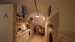 A narrow kitchen with a dining area, featuring a tiled floor, wooden cabinets, and a hanging light fixture. - Suite del Vico Family (Alberobello)