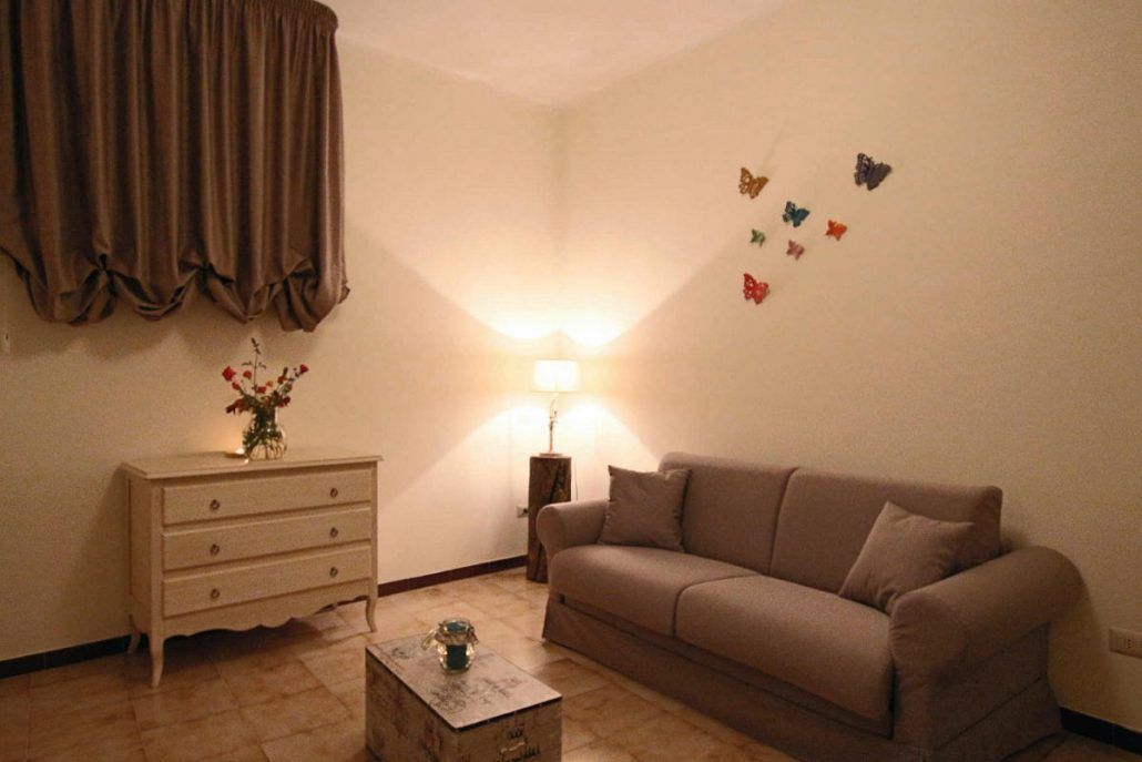 A living room with a beige sofa, a white dresser, a lamp, and butterfly wall decals.