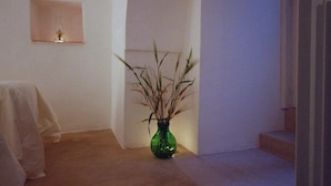 A hallway with a green vase of dried plants on the floor, a small shelf with a decorative item, and a staircase to the right. - Suite del Vico Family (Alberobello)