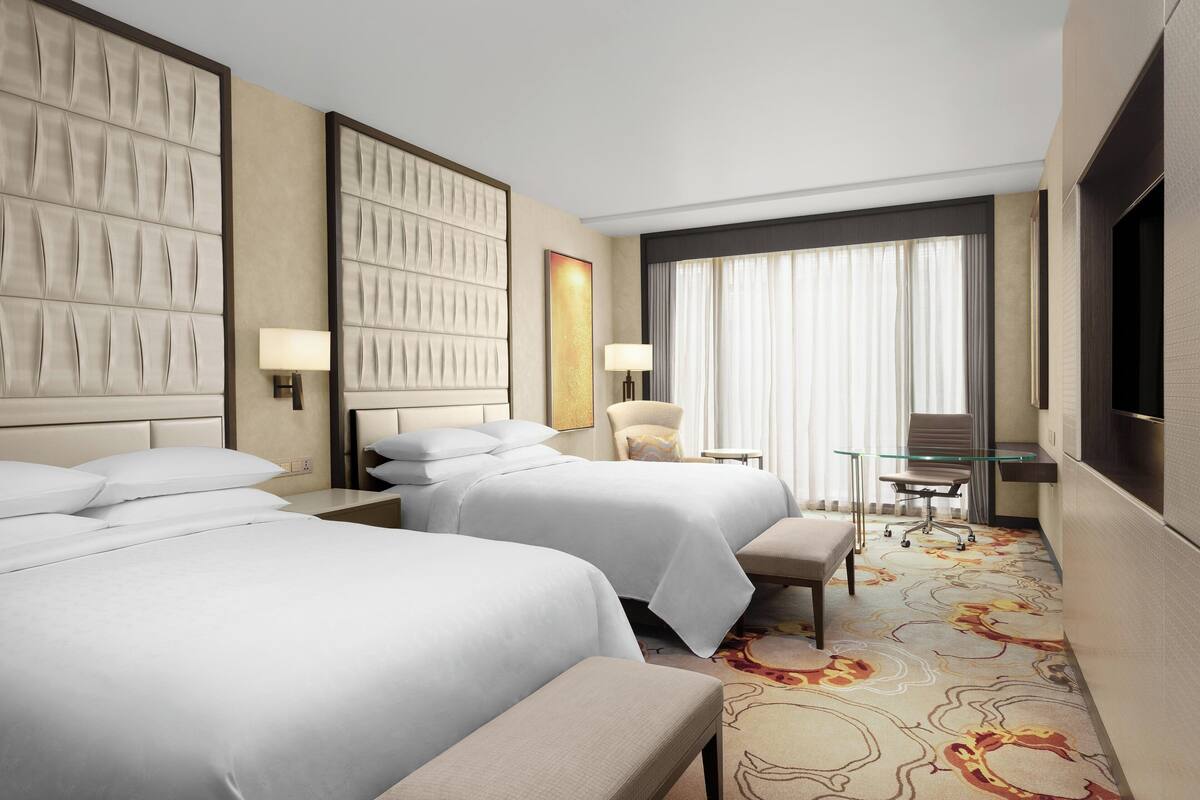 A hotel room with two beds, a desk, a chair, and a television.