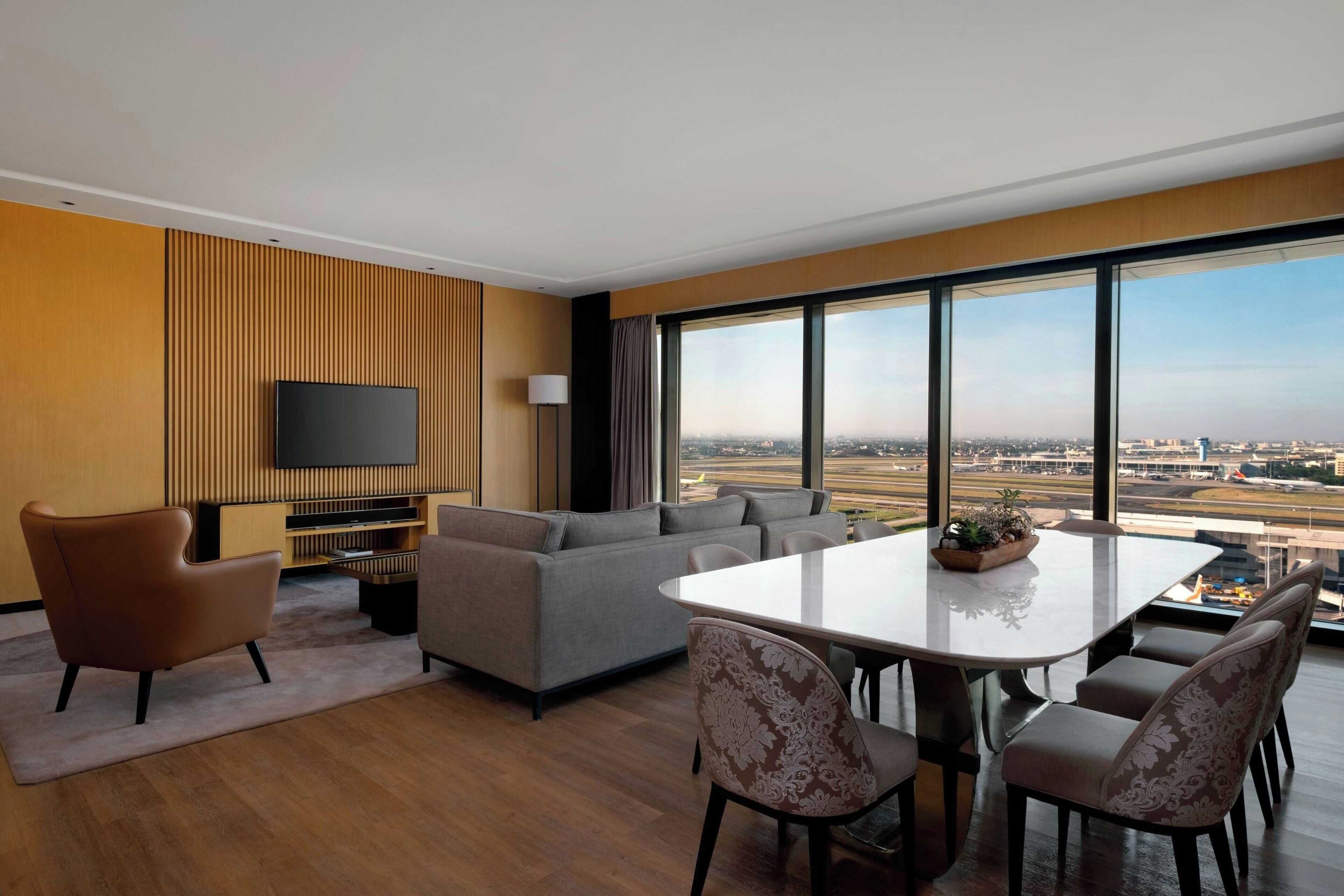 A modern living room with a large window, a flat-screen TV, a sofa, a dining table, and a coffee table.