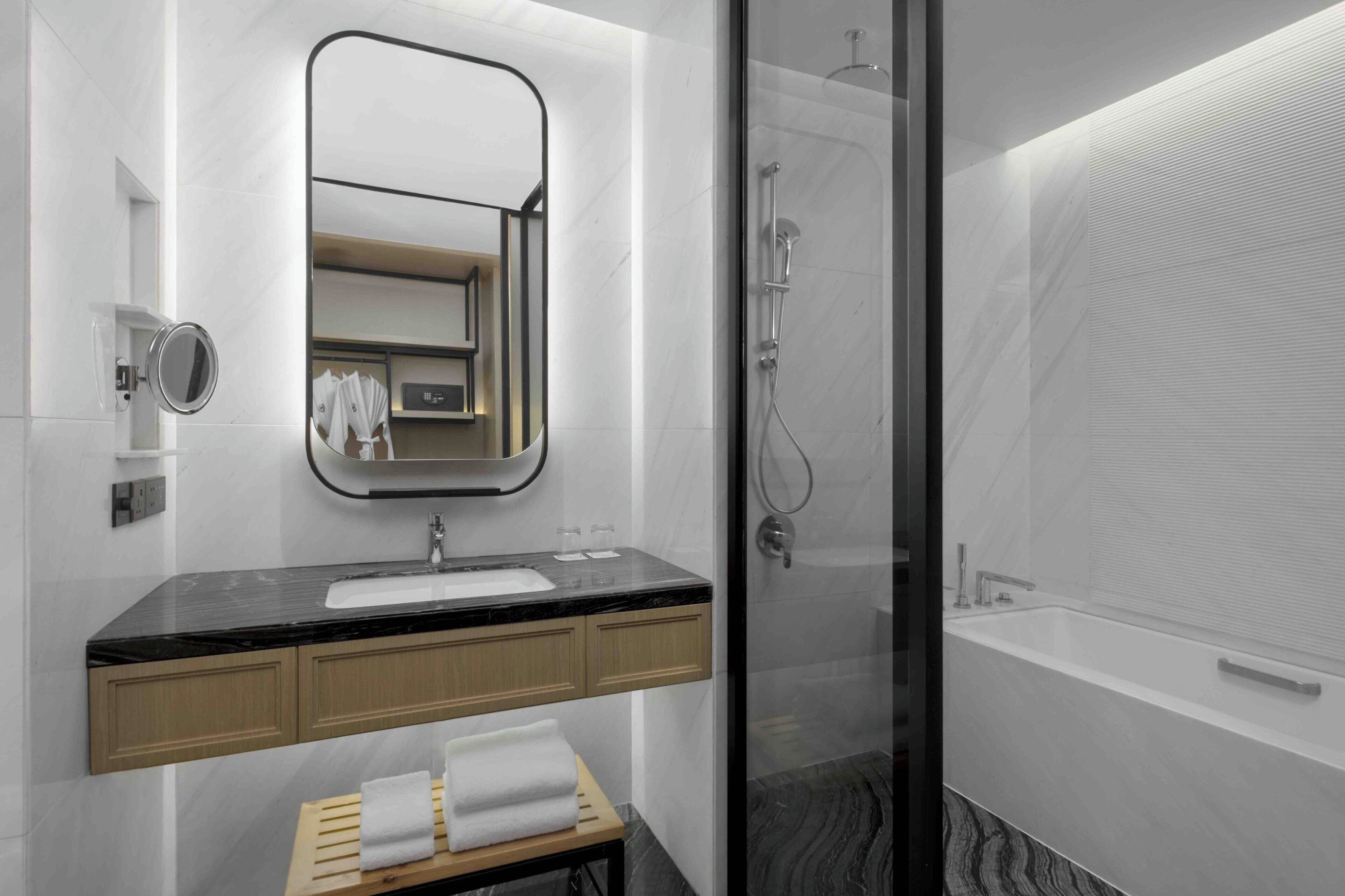 A modern bathroom with a black countertop sink, wooden cabinets, a mirror, a glass-enclosed shower, and a white bathtub.
