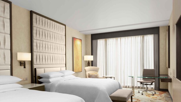 Una habitación de hotel con dos camas, una silla, un escritorio y un ventanal grande con cortinas.