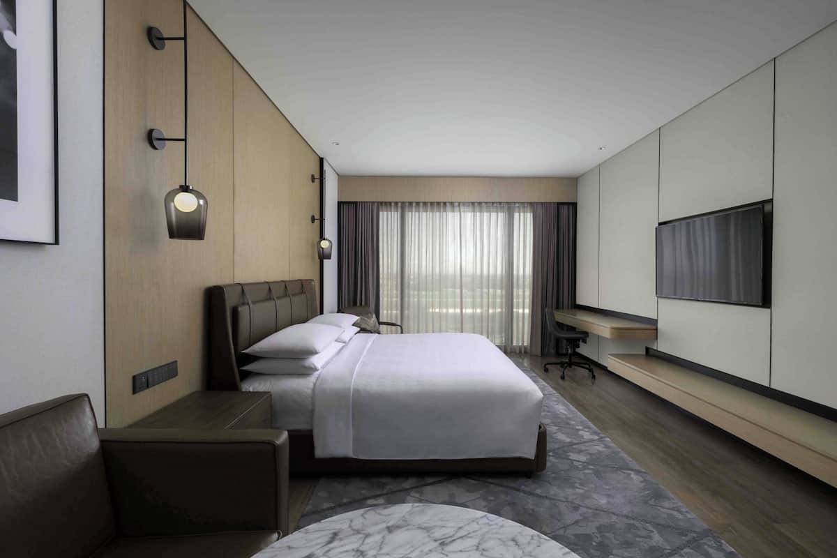 A hotel room with a large bed, a desk, a chair, a TV, and a window with curtains.