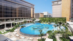 Un hotel con una amplia piscina exterior rodeada de sillones de descanso y vegetación, arquitectura moderna y cielo despejado.