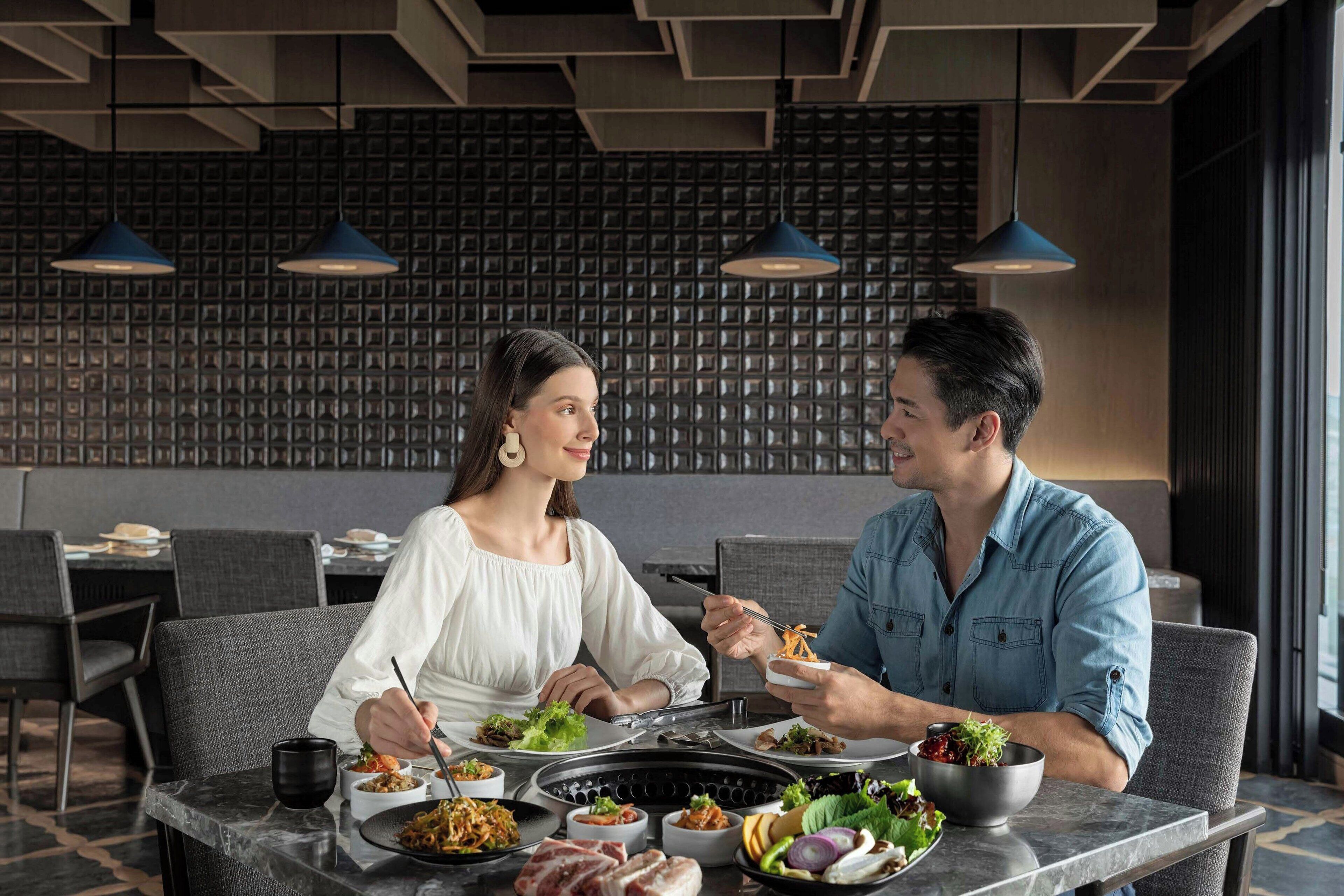 A modern dining area with a black grill table, various dishes, and two people dining.
