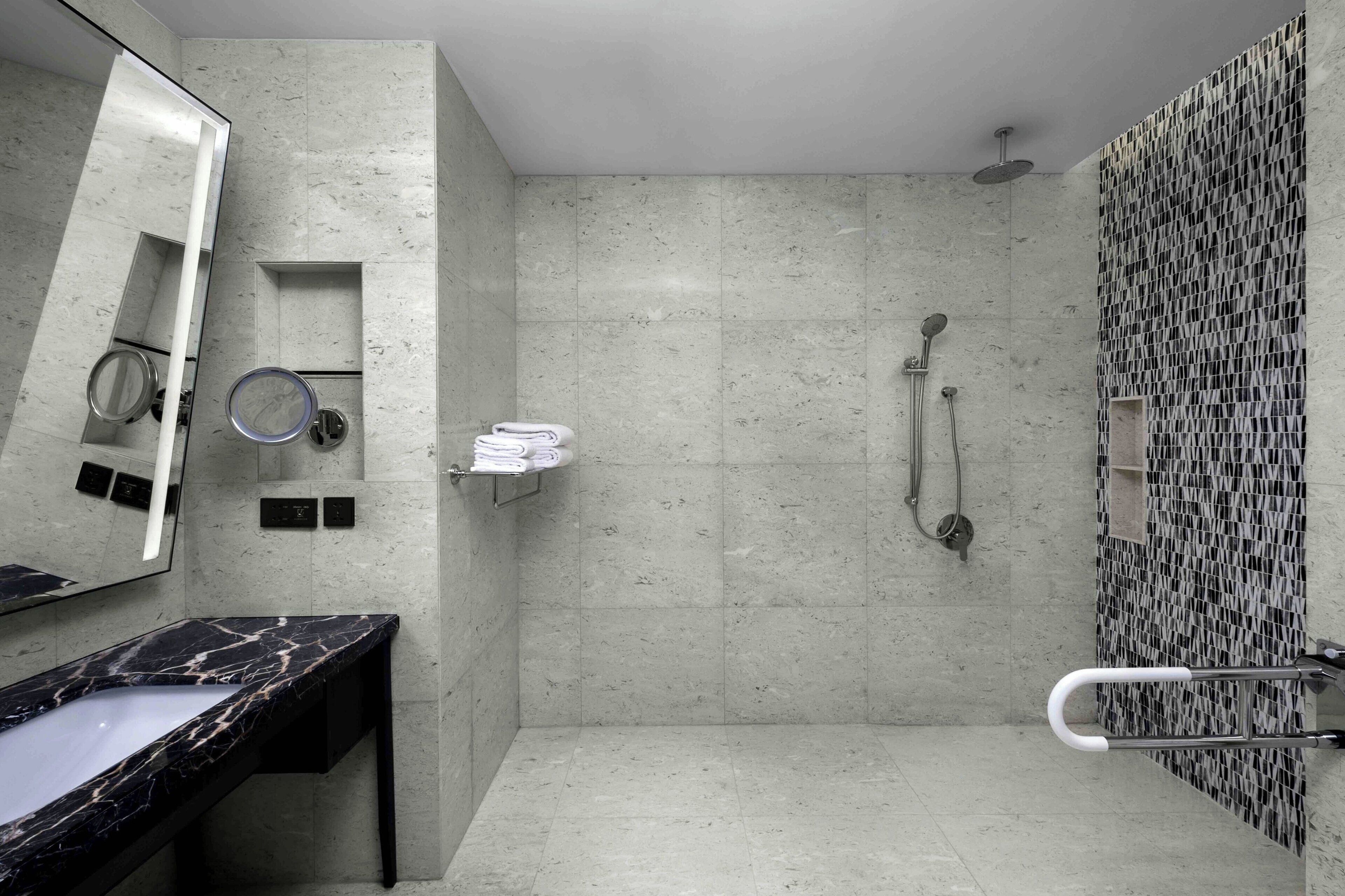 A modern bathroom with a marble sink, a shower with a rain showerhead, and a patterned wall.