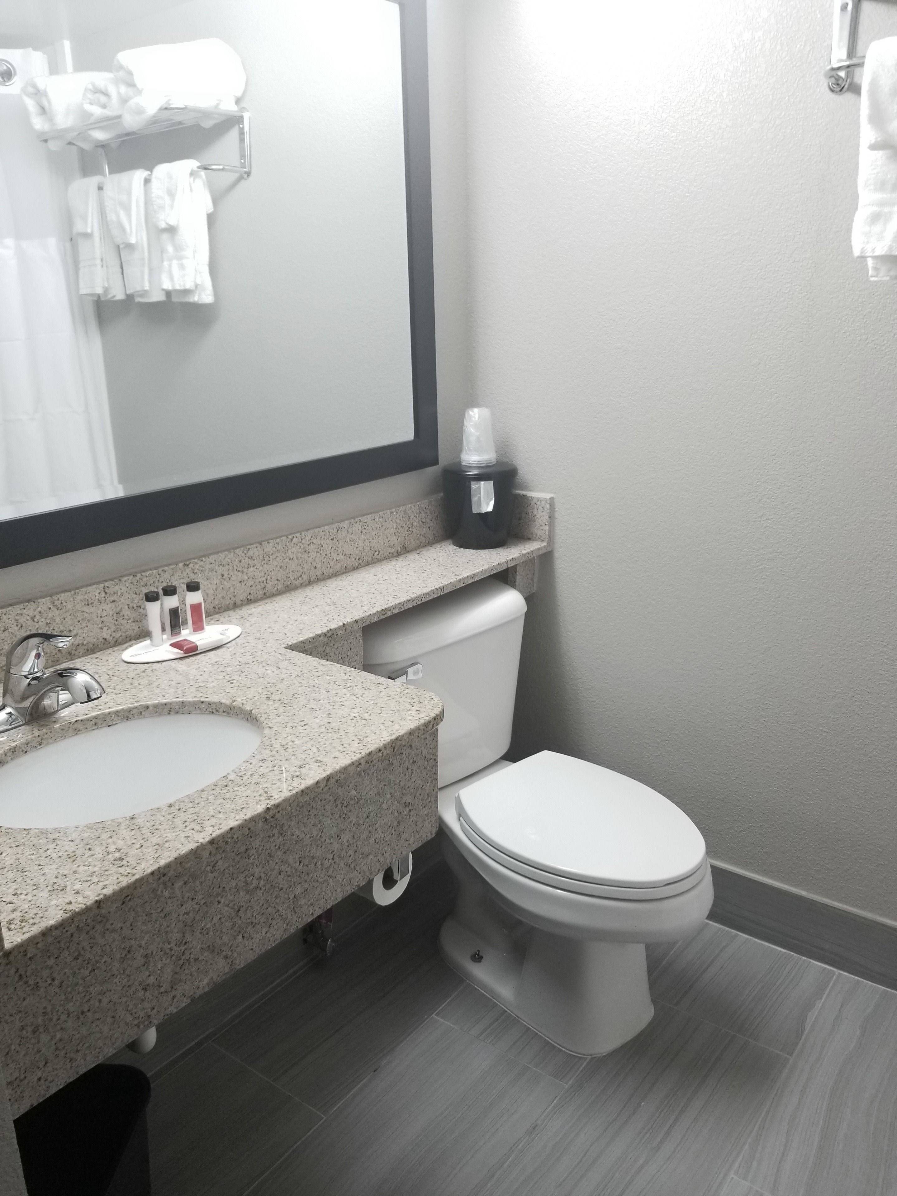 Een moderne badkamer met een wastafel met een granieten blad, een wit toilet en een grote spiegel.