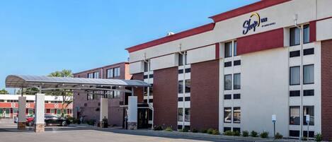 A hotel with a covered entrance, a parking lot, and a clear blue sky.