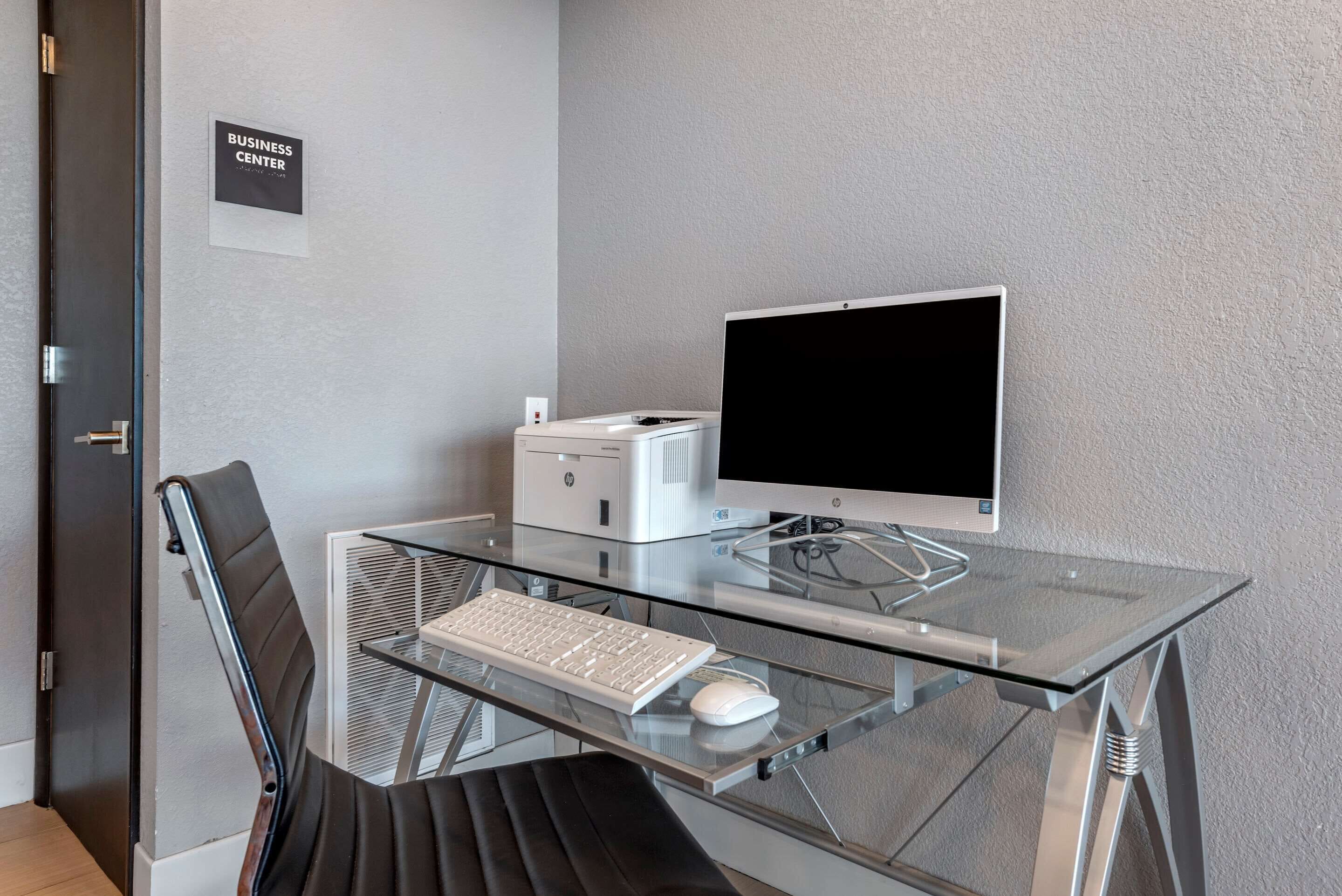 Un espace de bureau moderne avec un bureau en verre, un clavier blanc, un écran et une chaise.