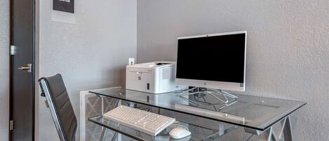 Un espace de bureau moderne avec un bureau en verre, un clavier blanc, un écran et une chaise.