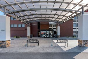 A covered entrance with a glass canopy, two benches, and a building entrance with a glass door.