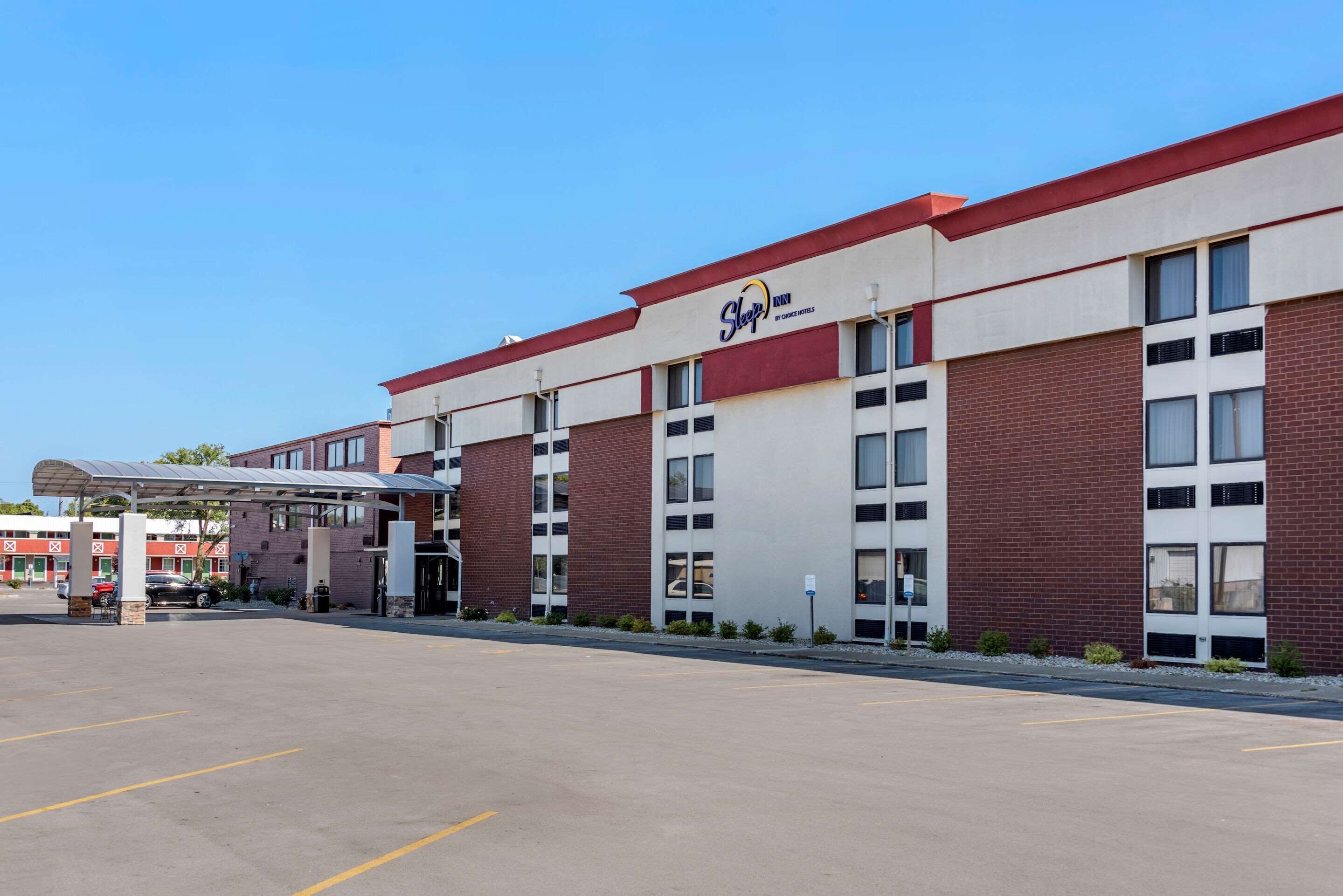 A hotel with a red and white facade, multiple windows, and a covered parking area.