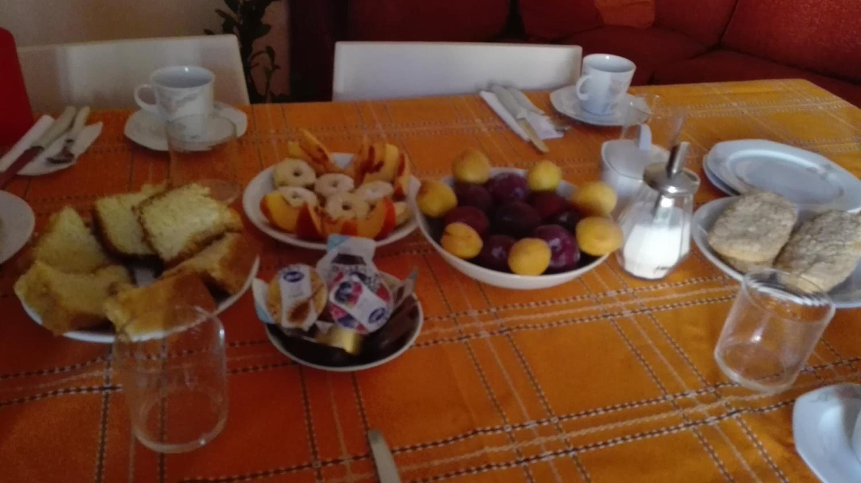 A breakfast table with plates of toast, fruit, and pastries, along with cups and a salt shaker.