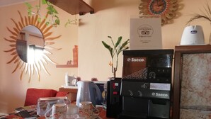 A hotel room with a coffee machine, a table with a tray of cups and saucers, a mirror with a sun design, and a certificate on the wall. - B&B Casa Mia (Alghero)