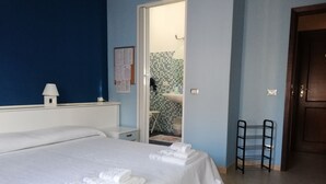 A hotel room with two beds, a small table, a chair, a door, and a bathroom visible through an open door. - B&B Casa Mia (Alghero)