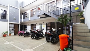 Un immeuble résidentiel à plusieurs étages, doté d’un escalier central, de plantes en pot et de motos garées.