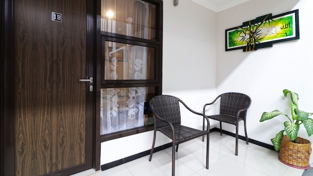 Une pièce avec une porte en bois sombre, deux fauteuils en osier, une plante en pot et une œuvre d’art encadrée accrochée au mur.