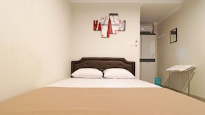 Un grand lit avec une tête de lit marron, des oreillers blancs et une couverture beige. Un tableau décoratif est accroché au mur au-dessus du lit, et un petit miroir se trouve sur le mur, à droite.