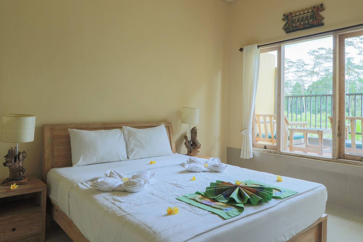 A neatly made bed with white linens and floral decorations, a wooden headboard, and a window with a view of greenery.