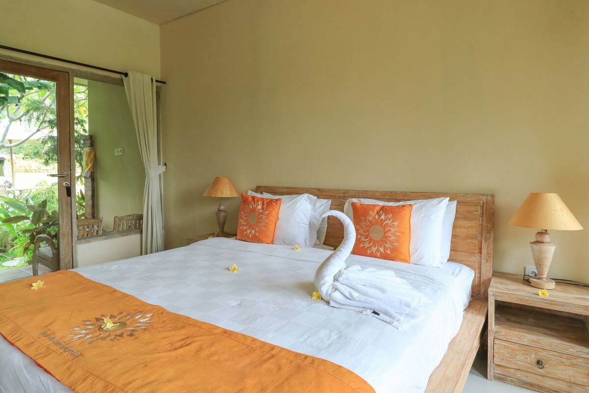 A hotel room with a bed, two nightstands, a wooden headboard, and a view through a glass door.
