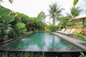 A rectangular pool with a surrounding garden, including palm trees and various plants. - Bali Sunshine Ubud (Sukawati)