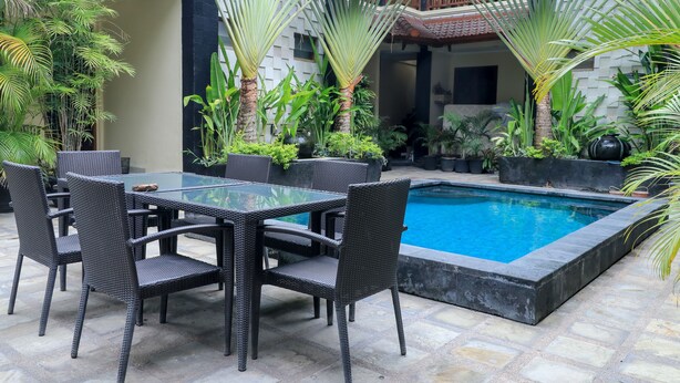 A poolside area with a table and chairs, surrounded by various potted plants. - Surfaris Inn on Poppies 2 (Kuta)