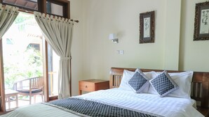 A bedroom with a bed, a nightstand, a chair, and a window with curtains. - Surfaris Inn on Poppies 2 (Kuta)
