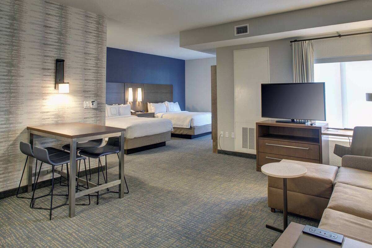 Une chambre d’hôtel comprenant un lit, un bureau avec des chaises, une télévision, un canapé et une petite table.