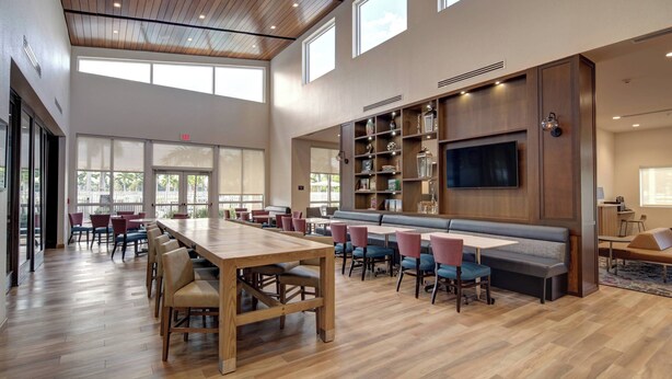 A spacious indoor area with a long wooden table, multiple seating options including chairs and a bench, and a large flat-screen TV mounted on the wall. - Residence Inn by Marriott Fort Lauderdale Coconut Creek (Coconut Creek)