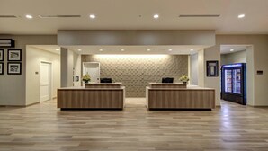A reception area with two wooden reception desks, a patterned wall, and a refrigerator with beverages. - Residence Inn by Marriott Fort Lauderdale Coconut Creek (Coconut Creek)