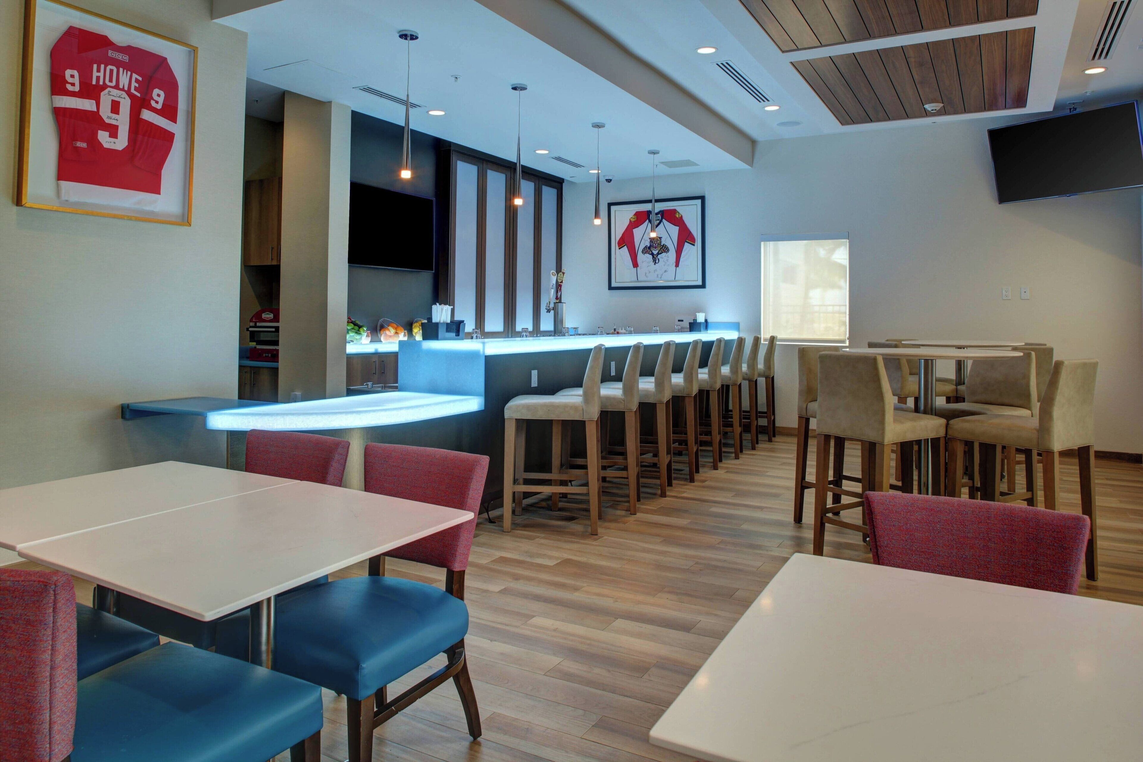 A modern restaurant with a bar area, multiple seating options including booths and high tables, and a sports jersey displayed on the wall.