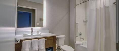 Un bagno moderno con lavandino, specchio e servizi igienici bianchi. Si nota una tenda da doccia e un box doccia in vetro.